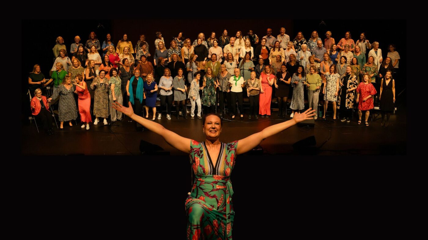 Kristina GIssler står framför en stor kör och sträcker ut armarna mot betraktaren