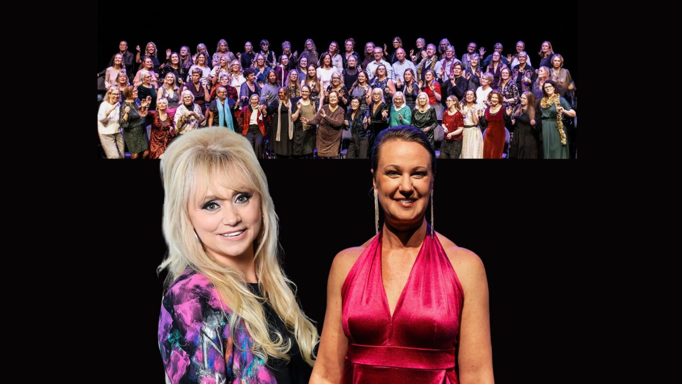 En stor kör i bakgrunden med två sångerskor i scenkläder i förgrunden