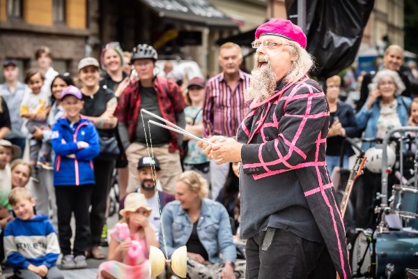 Man i stort skägg och rosa basker framträder med diabolokonster bland publik utomhus
